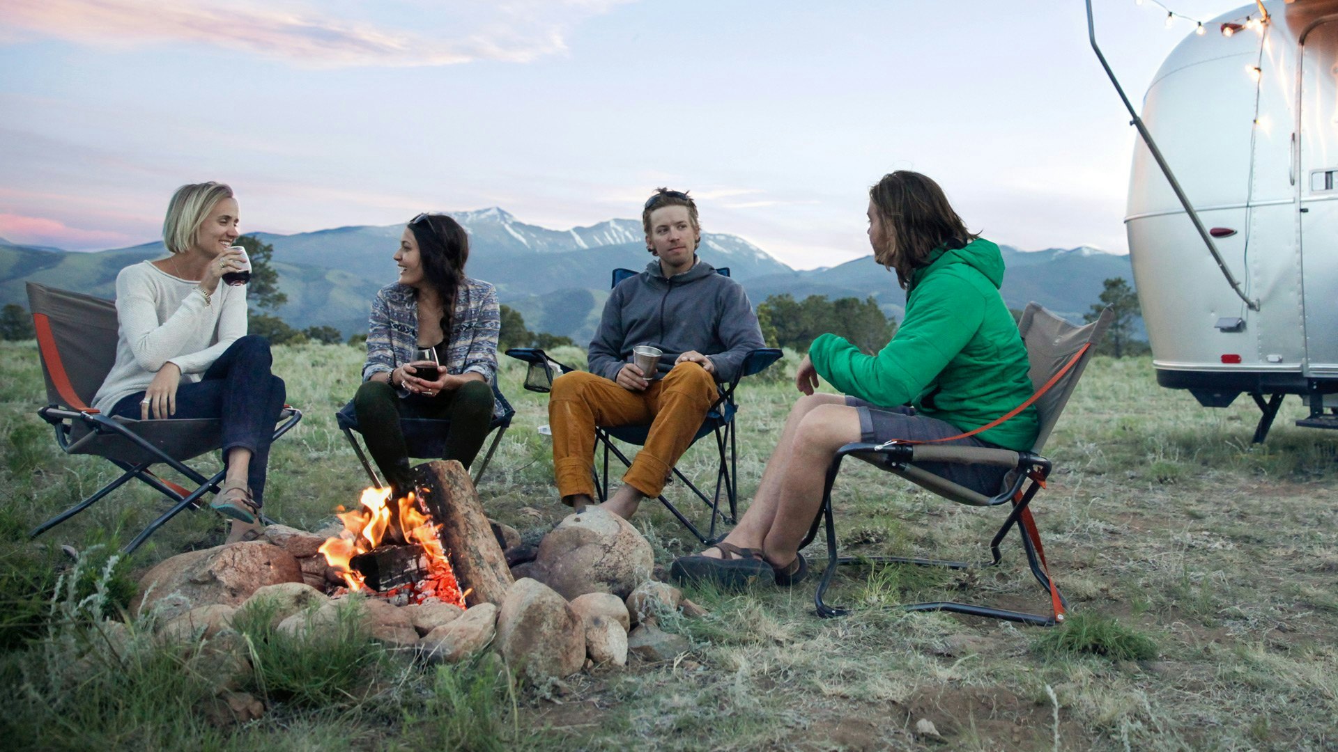 four millennials around a campfire with airstream in the background