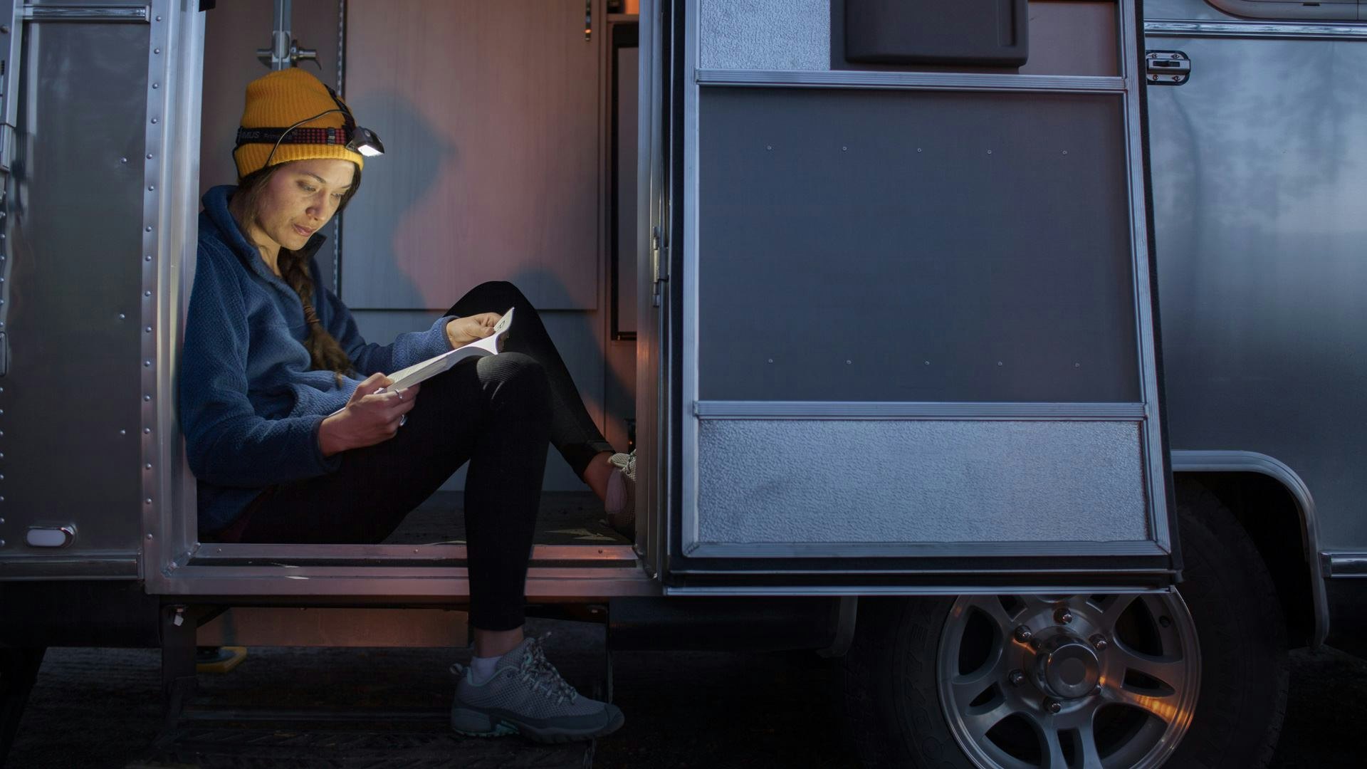 girl sitting in door of airstream with flashlight