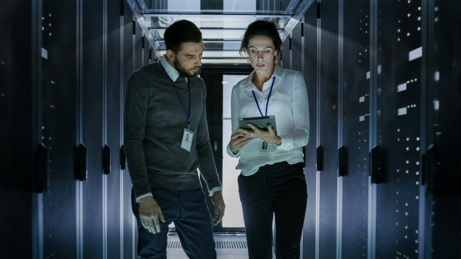 two technology workers walking through computer server room looking at an ipad